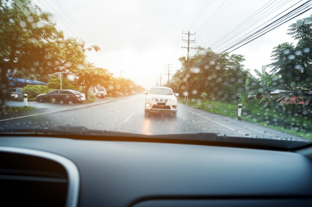 A car driving on a wet road during the Thai rainy season, illustrating the challenge of protecting paintwork.